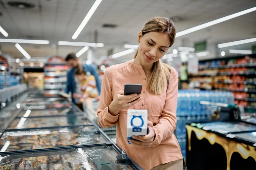 młoda kobieta trzyma w dłoni produkt i skanuje kod, by przejść do cyfrowego paszportu produktu