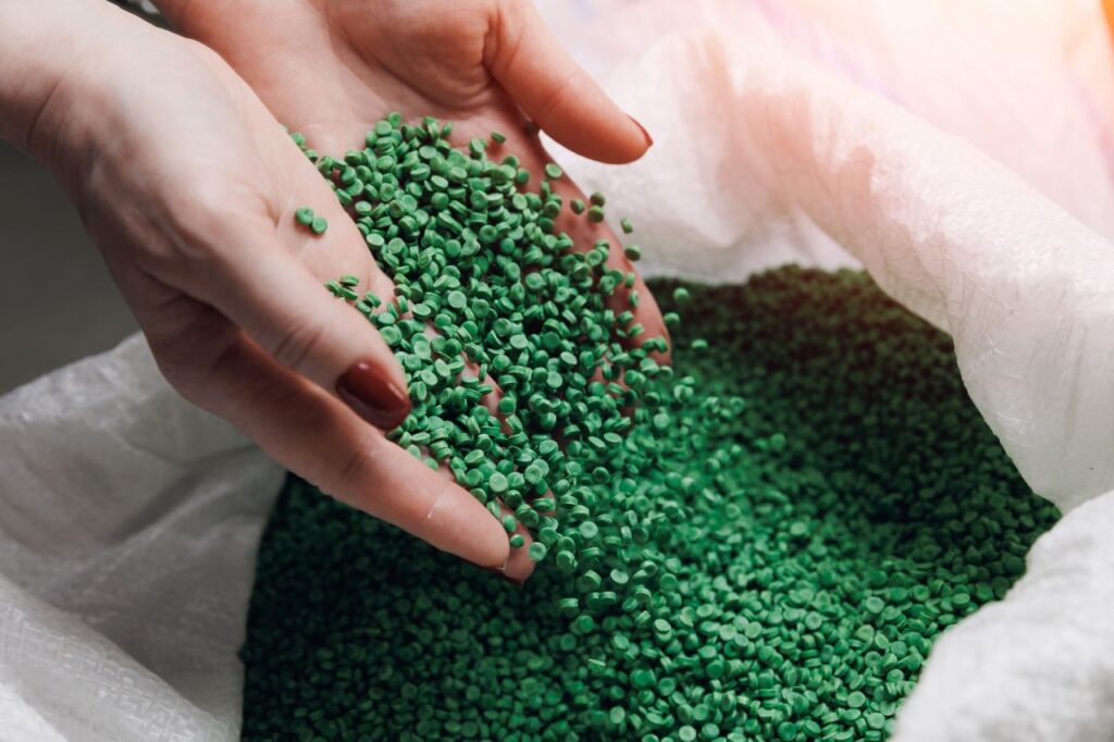 damskie dłonie wsypują zielony recyklat tworzyw sztucznych do białego worka