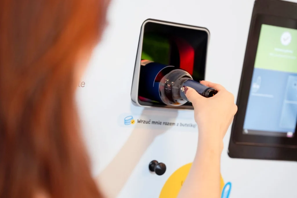 kobieta wrzuca butelkę zwrotną do butelkomatu należącego do polskiego systemu kaucyjnego, by odzyskać kaucję