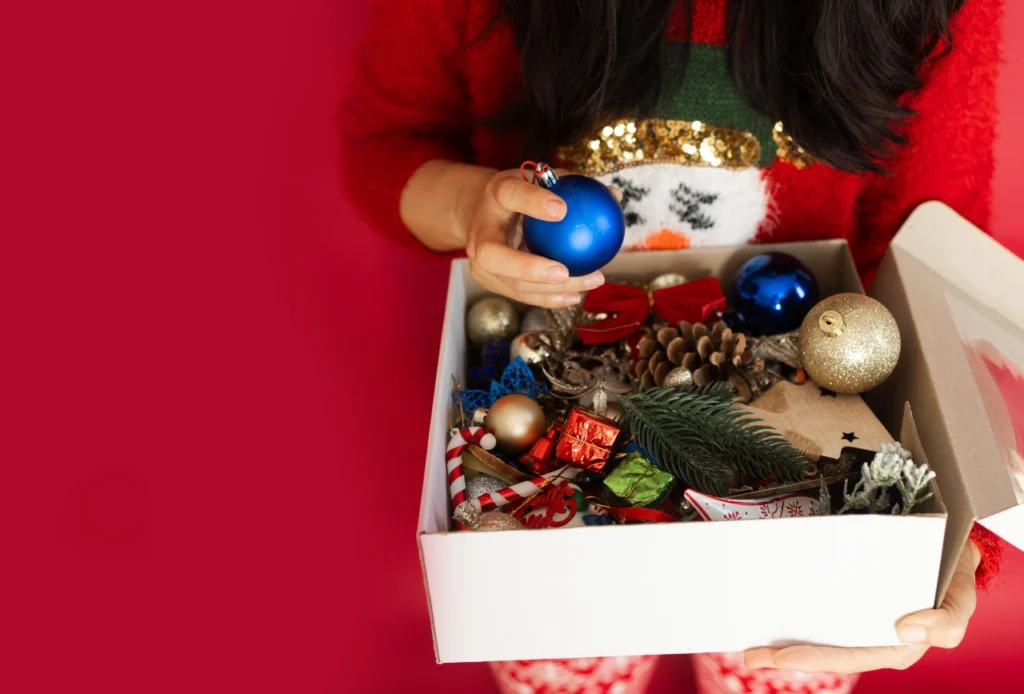 kobieta trzyma pudełko starych ozdób choinkowych i zastanawia się, gdzie je wyrzucić